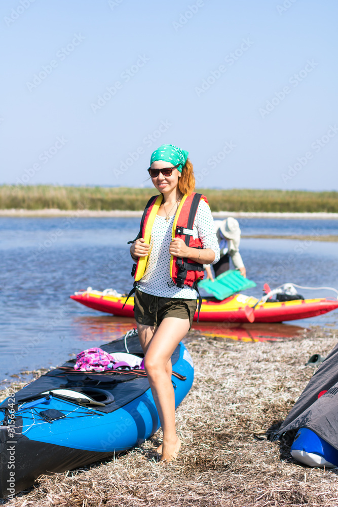 Obraz premium red-haired girl in red life vest standing near expedition kayaks