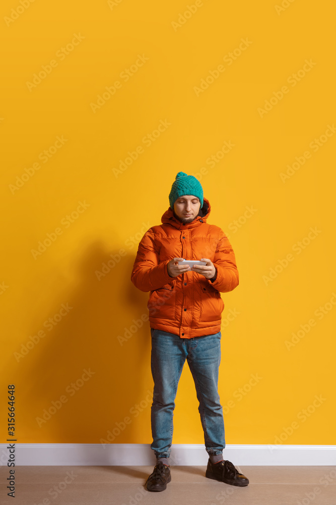 Using gadgets anywhere. Young caucasian man using smartphone, serfing, chatting, betting. Full length portrait isolated on yellow background. Concept of modern technologies, millennials, social media.