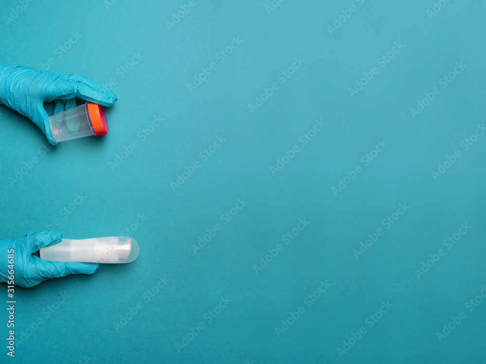 Doctor hands in latex rubber gloves holding a plastic container and a lubricant of liquids on a blue background with place for text Doctor hands in latex rubber gloves holding a plastic container and a lubricant of liquids on a blue background with place for text