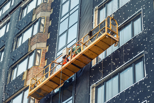 Obraz na plátně Suspended construction craddle near wall of hightower residentaial building with insulation and ventilated facade on construction site