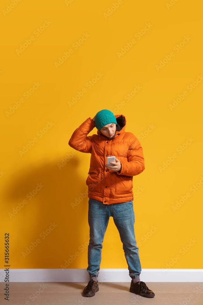 Disappointed. Young caucasian man using smartphone, serfing, chatting, betting. Full length portrait isolated on yellow background. Concept of modern technologies, millennials, social media. Disappointed. Young caucasian man using smartphone, serfing, chatting, betting. Full length portrait isolated on yellow background. Concept of modern technologies, millennials, social media.