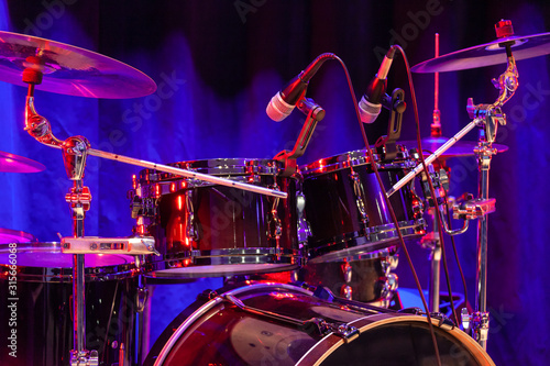 Drum set with bass drum, tom-toms, cymbals and microphones on the stage with blue-red illumination