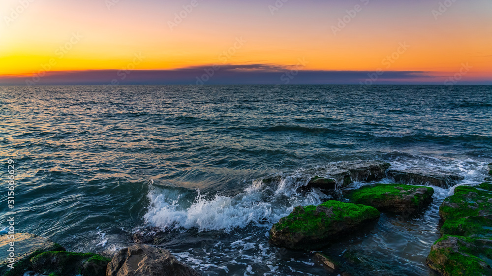Waves crashing on the rocky seashore at sunset