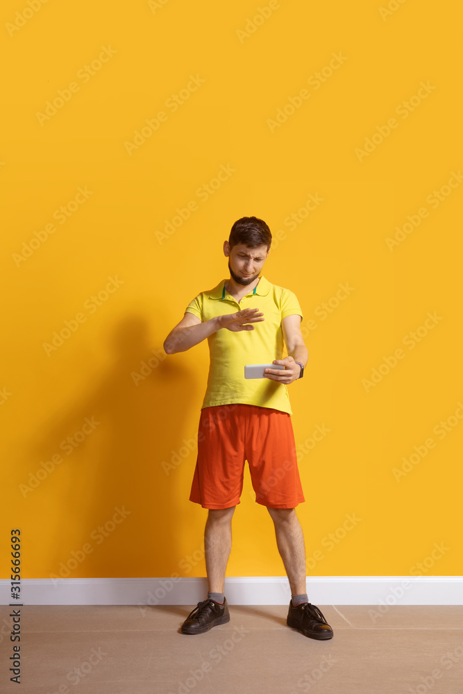 Shocked, wondered. Young caucasian man using smartphone, serfing, chatting, betting. Full length portrait isolated on yellow background. Concept of modern technologies, millennials, social media. Shocked, wondered. Young caucasian man using smartphone, serfing, chatting, betting. Full length portrait isolated on yellow background. Concept of modern technologies, millennials, social media.