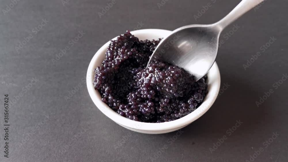 The process of laying black caviar in a white plate. The process of laying black caviar in a white plate.