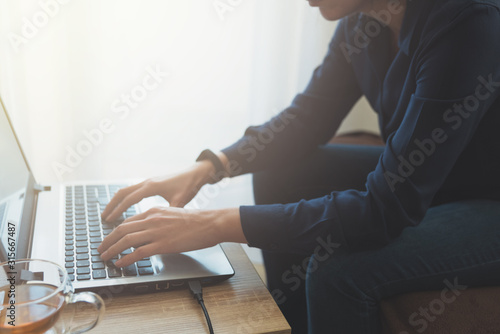Young adult using laptop and typing on keyboard. Soft focus. Job at home. Female freelancer.