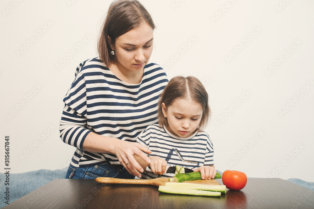 Young mother teaches her little daughter to cut vegetables Young mother teaches her little daughter to cut vegetables