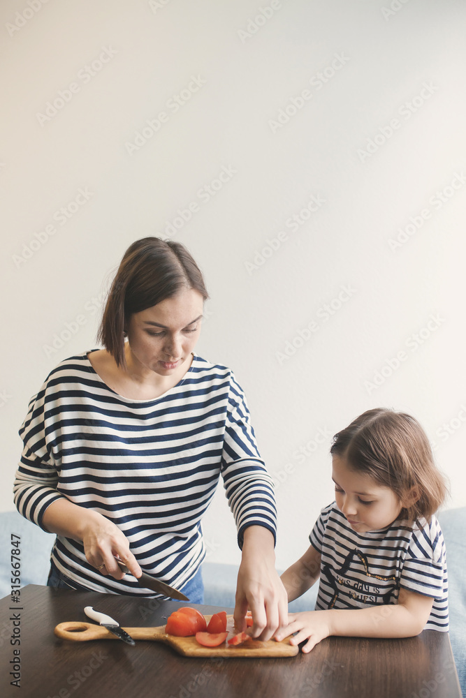 Fototapeta premium Young mother teaches her little daughter to cut vegetables
