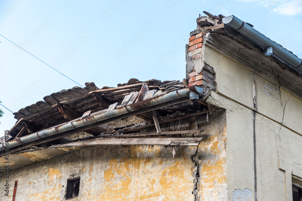 Remains of hurricane or earthquake aftermath disaster damage on ruined old houses with collapsed roof and wall with dust in the air