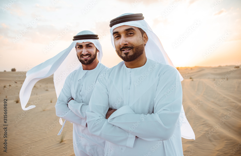 Naklejka premium Two business men wearing traditional uae white kandura spending time in the desert of Dubai