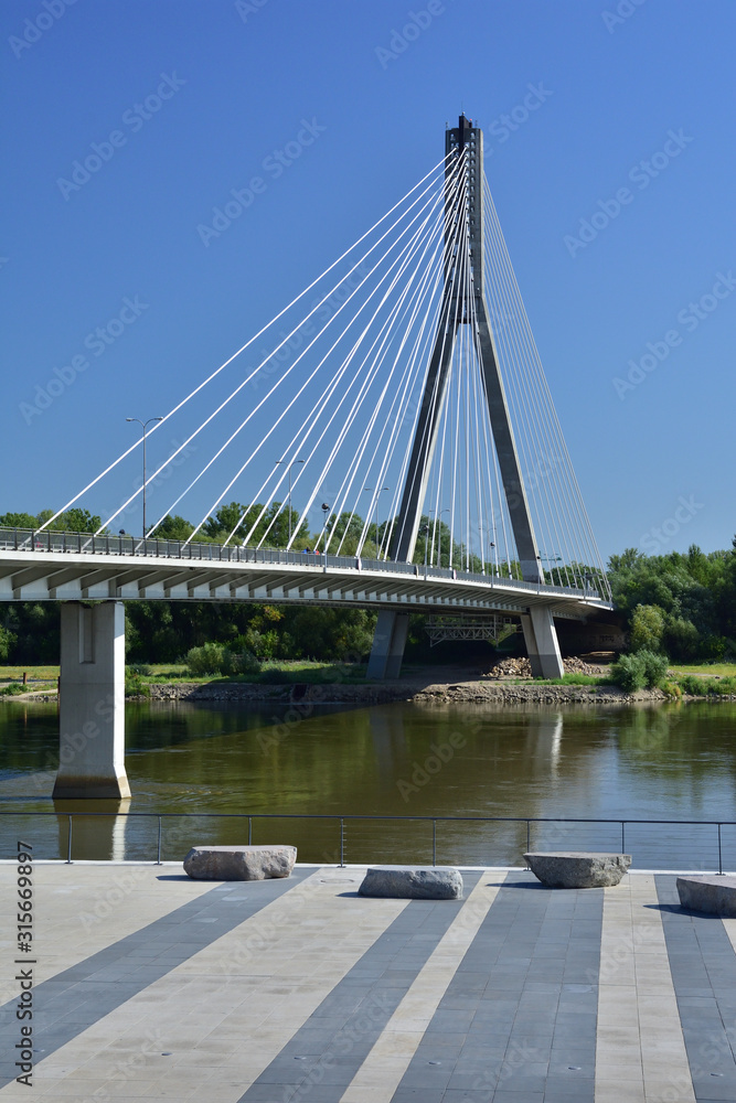 Naklejka premium Wiszący most nad rzeką na bezchmurnym niebie w gorący, letni dzień.
