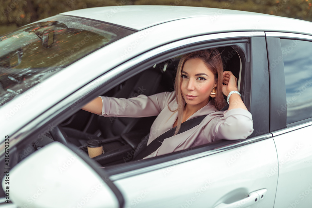 Beautiful girl in a car interior driving. In summer in city. Happy smiles. Car sharing car for rent. Business sedan in white. Parking in parking lot. Emotions of comfort pleasure, close-up.