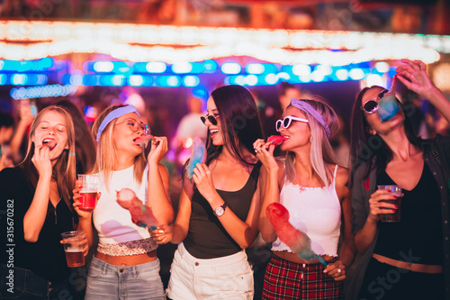 Billede på lærred Female friends eating cotton candy and drinking beer in amusement park