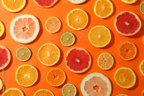 Many citrus fruits slices on orange background, top view