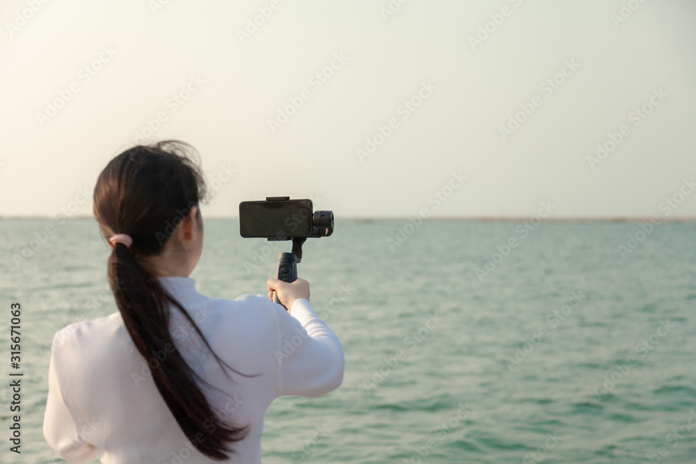 Obraz premium Blogger Asian woman record vlog video and sharing content on streaming platform with Social Network. female enjoy in front of camera using mobile phone make vlogging live feeds on social media network