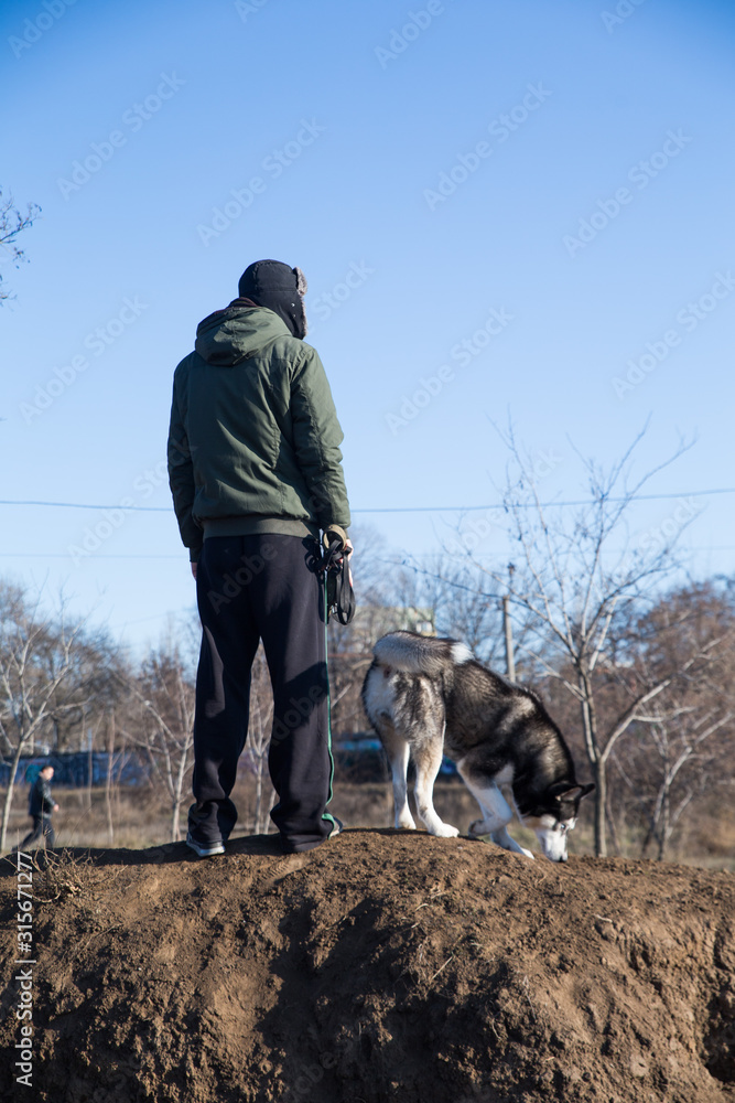 A young man in warm clothes is standing on the street with his husky dog, black and white A young man in warm clothes is standing on the street with his husky dog, black and white