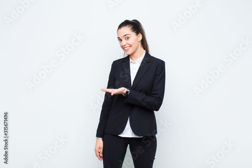 young pretty woman smiling cheerfully, feeling happy and showing a concept in copy space with palm of hand business concept