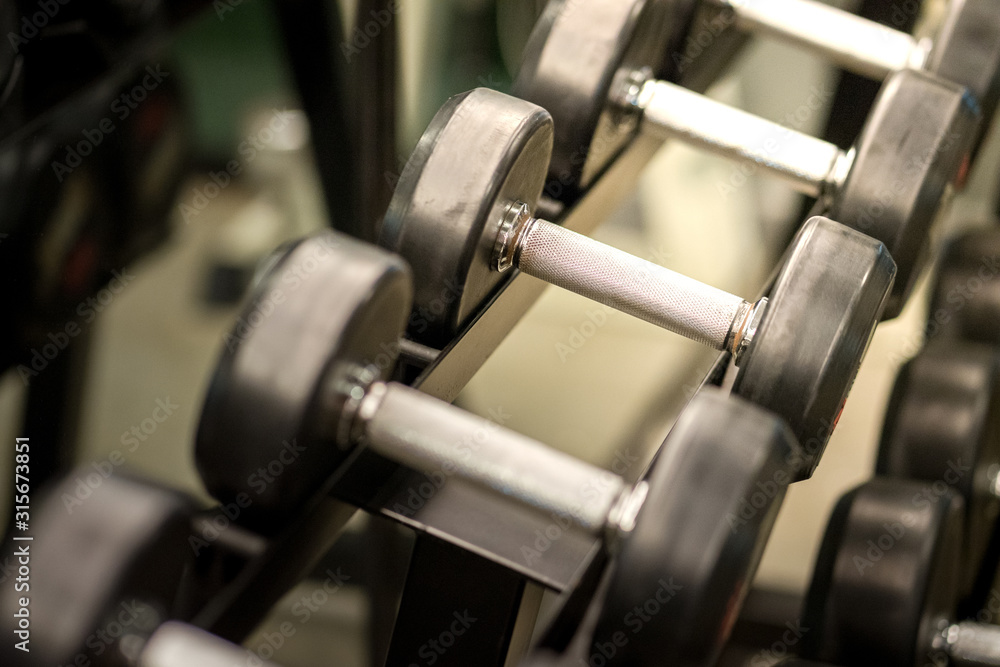 Dumbbell weight, equipment for workout, there are available on row rack in fitness gym. Selected focus on metal handle.