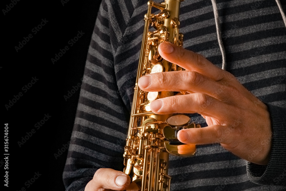 Obraz premium soprano saxophone in the hands of a guy on a black background