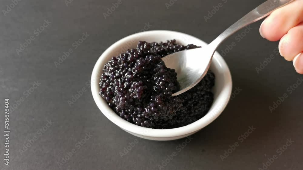 The process of laying black caviar in a white plate. The process of laying black caviar in a white plate.