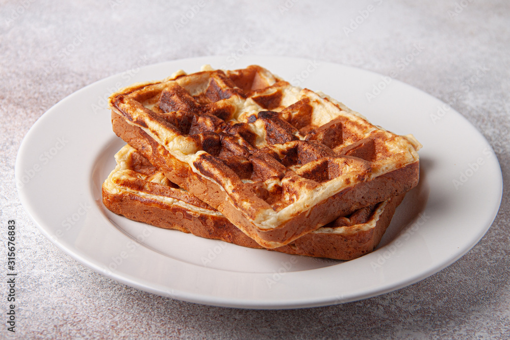 Belgian waffles on a white plate and craft background. Tasty waffer close up. Belgian waffles on a white plate and craft background. Tasty waffer close up.