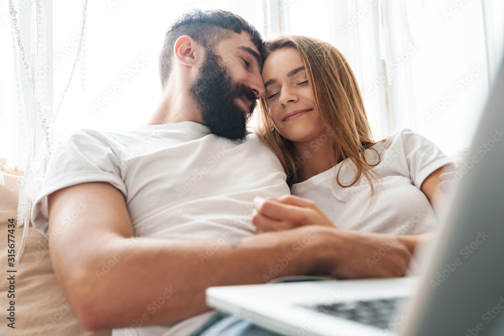 Image of romantic calm couple using laptop and hugging while sitting Image of romantic calm couple using laptop and hugging while sitting