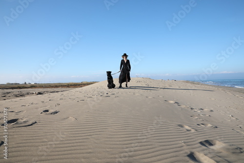 Young woman standing on top of a sandy beach with dog. Outdoor.