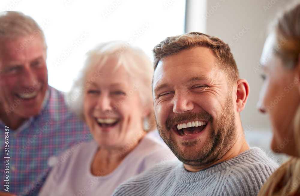 Senior Parents With Adult Offspring Sitting On Sofa At Home Talking And Laughing Senior Parents With Adult Offspring Sitting On Sofa At Home Talking And Laughing