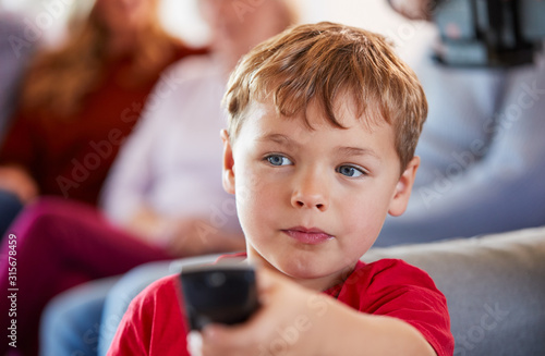 Boy Watching Television At Home With Multi-Generation Family Relaxing In Background