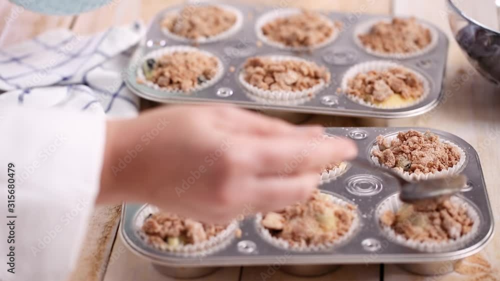 Scooping cinnamon and sugar topping on blueberry muffin batter. Scooping cinnamon and sugar topping on blueberry muffin batter.