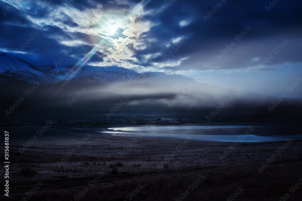 The predawn fog over the Dzhangyskol lake in the tract Eshtykol and the North Chuysky ridge in the moonlight. Russia, Altai Republic