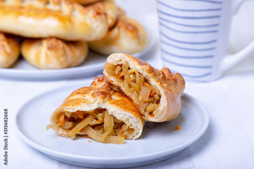 Pies (pirozhki) with cabbage. Homemade baking. Traditional Russian and Ukrainian cuisine. In the background is a dish with pies. Close-up. Pies (pirozhki) with cabbage. Homemade baking. Traditional Russian and Ukrainian cuisine. In the background is a dish with pies. Close-up.