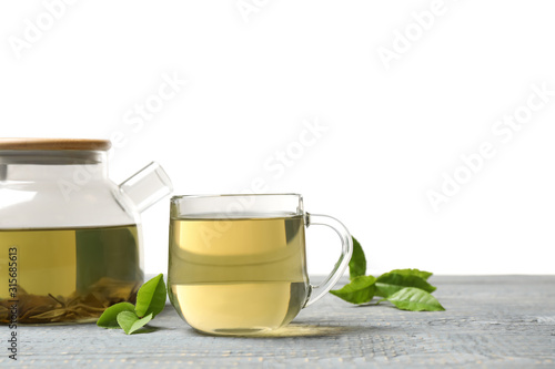 Cup of green tea, pot and leaves on grey wooden table