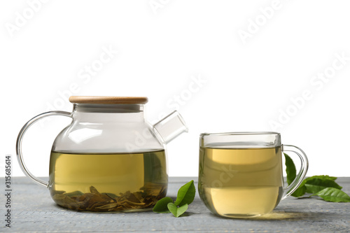 Cup of green tea, pot and leaves on grey wooden table
