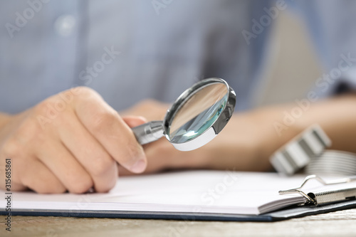 Woman using magnifying glass at table, closeup