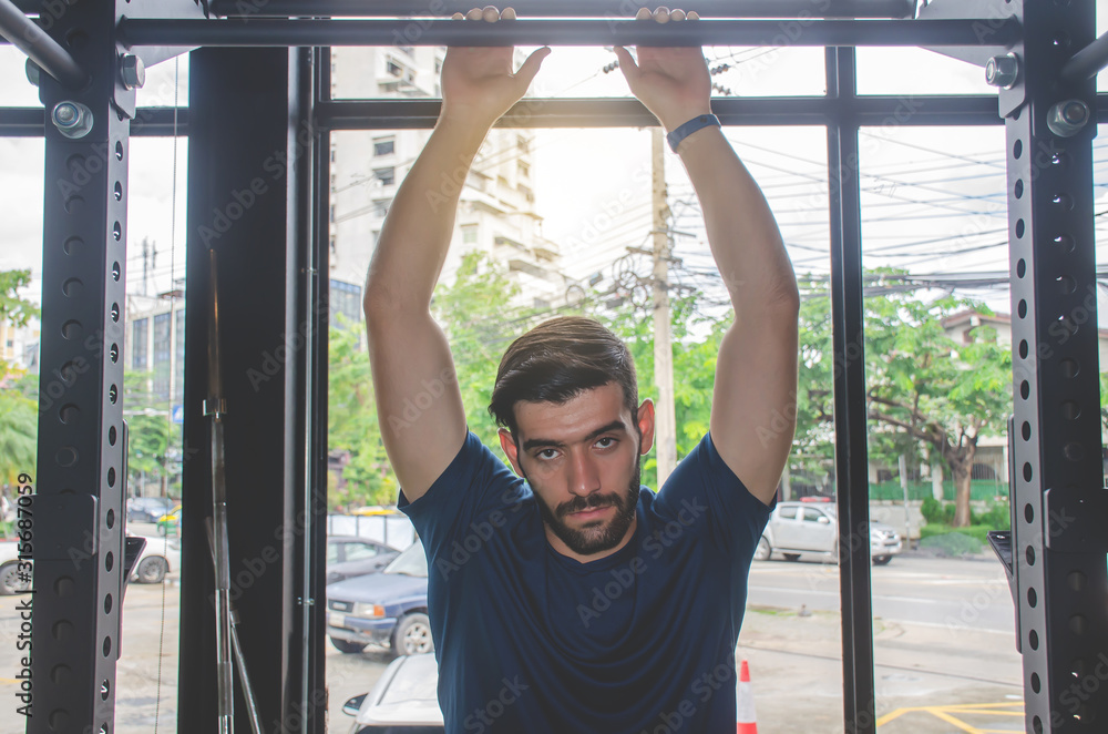 Fototapeta premium fitness, sport, training and lifestyle concept - Portrait of handsome strong athletic man exercising on horizontal bar in fitness gym and looking at camera.