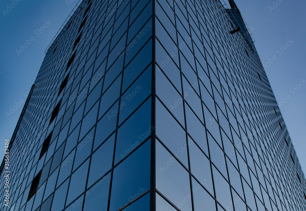 A symmetrical corner of a modern skyscraper fragment with glass panels and blue sky
