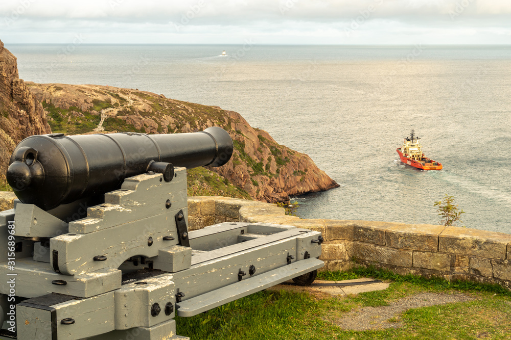 A modern deep water drilling rig support ship going out to sea under the watchful old cannon from the Queen's Battery #4, St. John's, Newfoundland