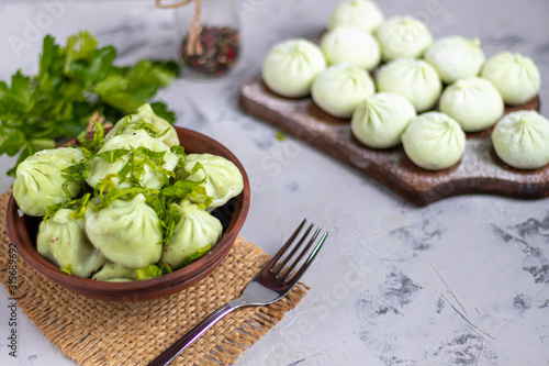 Boiled khinkali made of dough with spinach. Garnished with Red Chilli, Dill and Parsley. On a light gray background under