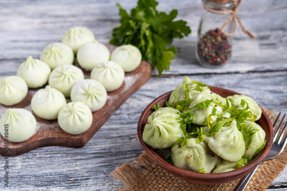 Boiled khinkali made of dough with spinach. Garnished with Red Chilli, Dill and Parsley. On a light gray background under Boiled khinkali made of dough with spinach. Garnished with Red Chilli, Dill and Parsley. On a light gray background under