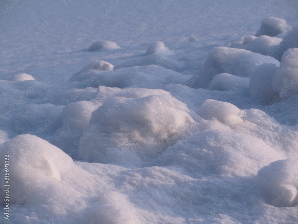 White winter background. Snow surface in perspective. Lumps of snow on the frozen surface of the lake. Lumps of snow in the rays of the setting sun. Winter snowy landscape. White winter background. Snow surface in perspective. Lumps of snow on the frozen surface of the lake. Lumps of snow in the rays of the setting sun. Winter snowy landscape.