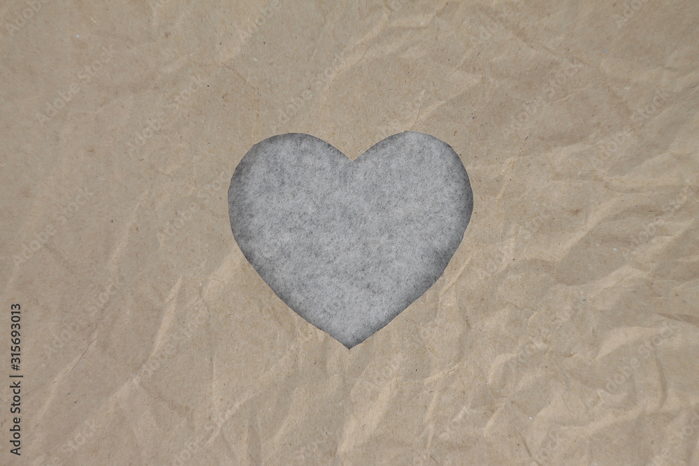 Fototapeta premium Gray felt heart on craft paper. Crumpled paper texture. Valentine's day stock photo for web, print and wallpaper. With empty space for text.