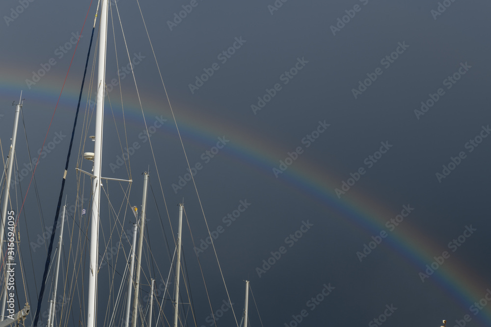 Beautiful rainbow on stormy sky in marina with sailing and motor yachts and boats. Beautiful rainbow on stormy sky in marina with sailing and motor yachts and boats.