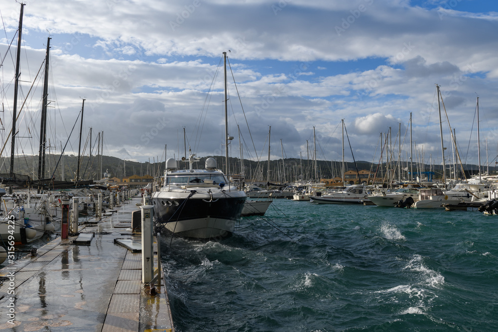 Beautiful rainbow on stormy sky in marina with sailing and motor yachts and boats.