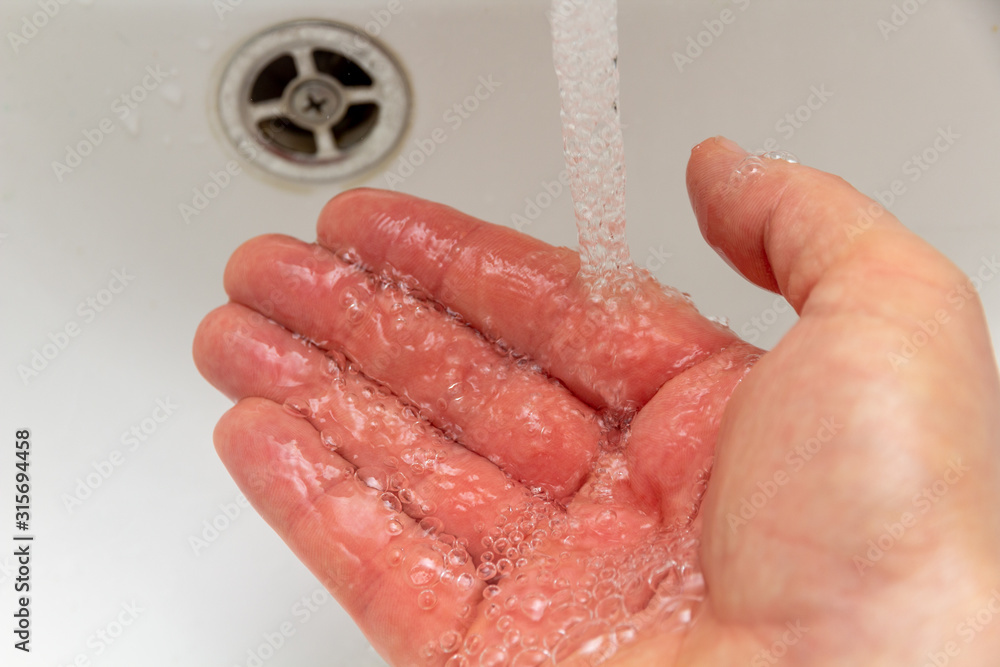 Fototapeta premium Mann hält seine Hand unter laufenden Wasserhahn