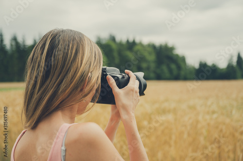 Young woman taking photo of beautiful wheat field