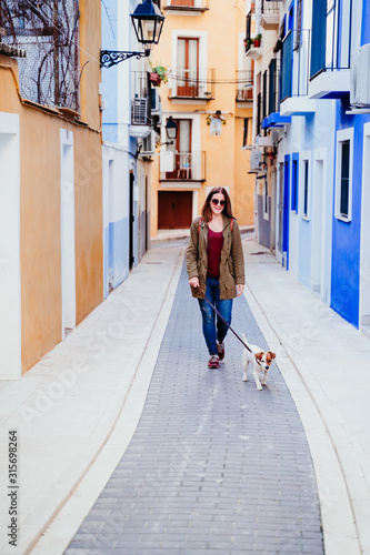 young woman and her cute jack russell dog walking by a colorful street at the city. travel concept