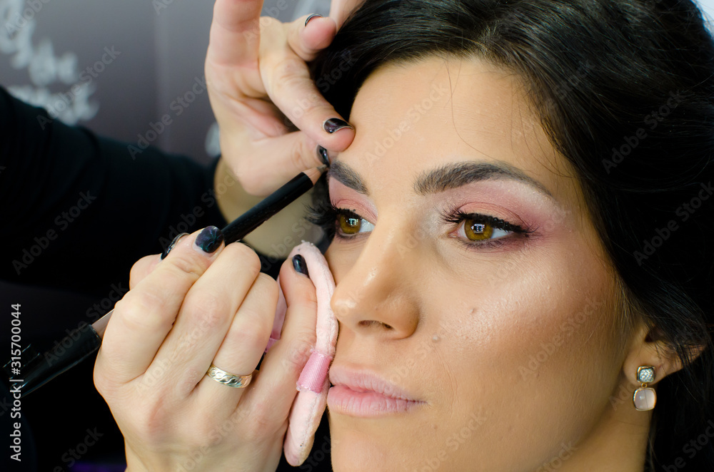 Make-up artist applying eye shadow on eyebrow to customer with eyebrows pen. Profile of beautiful blacked hair young woman in beauty studio, close up Make-up artist applying eye shadow on eyebrow to customer with eyebrows pen. Profile of beautiful blacked hair young woman in beauty studio, close up