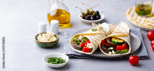 Wrap sandwich with grilled vegetables and feta cheese on a plate. Grey background.