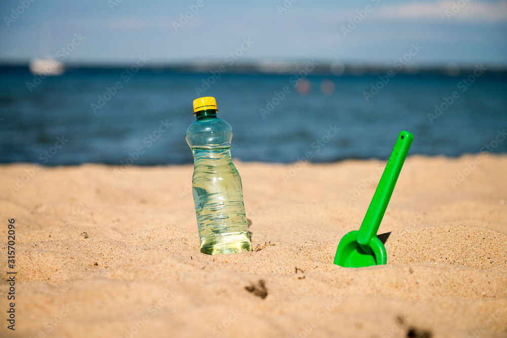 Plastic Bottle of fresh water is on the sand by the sea. Drinking water in bottle on sand on beach. Bottle of fresh water is on the sand by the sea. Bottled water on a hot day at the beach Plastic Bottle of fresh water is on the sand by the sea. Drinking water in bottle on sand on beach. Bottle of fresh water is on the sand by the sea. Bottled water on a hot day at the beach